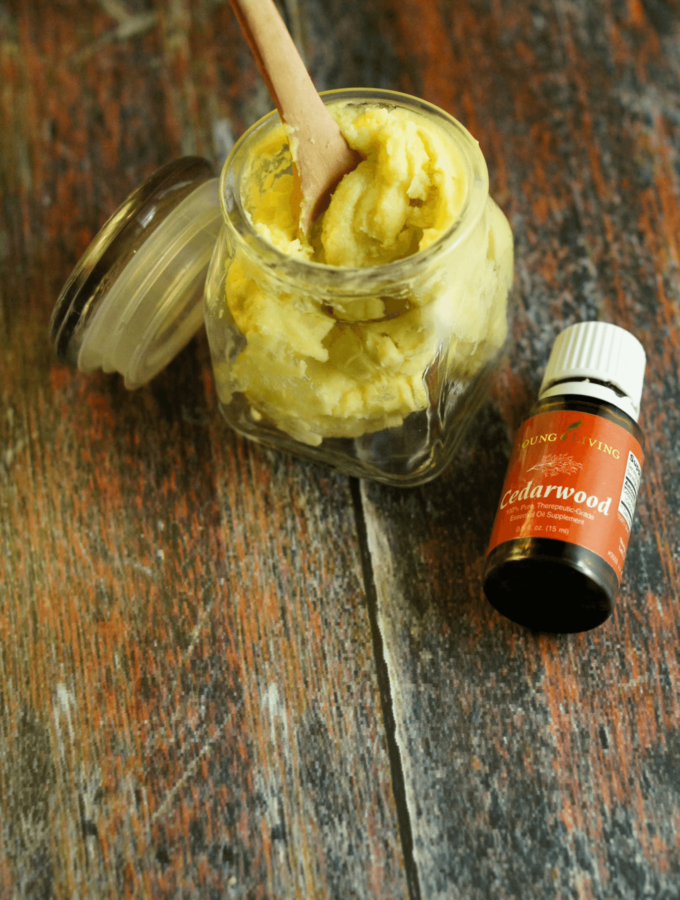 A jar of lotion with a small wooden spoon infused with a bottle of cedarwood essential oil on a wooden background.