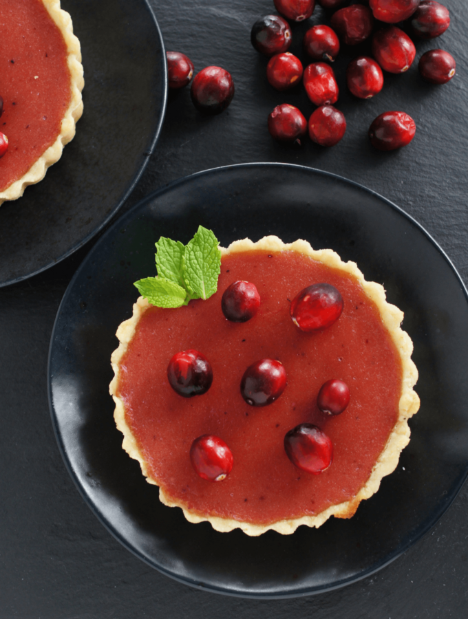 A healthy cranberry curd tart on a black plate with cranberries and mint