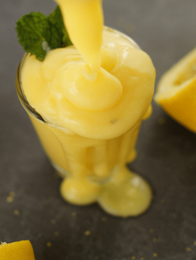Healthy lemon curd being poured into a shot glass with lemons in the background.