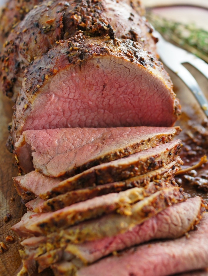 A medium rare sliced eye of round roast beef on a cutting board with all the juices, covered in a delicious dry rub.