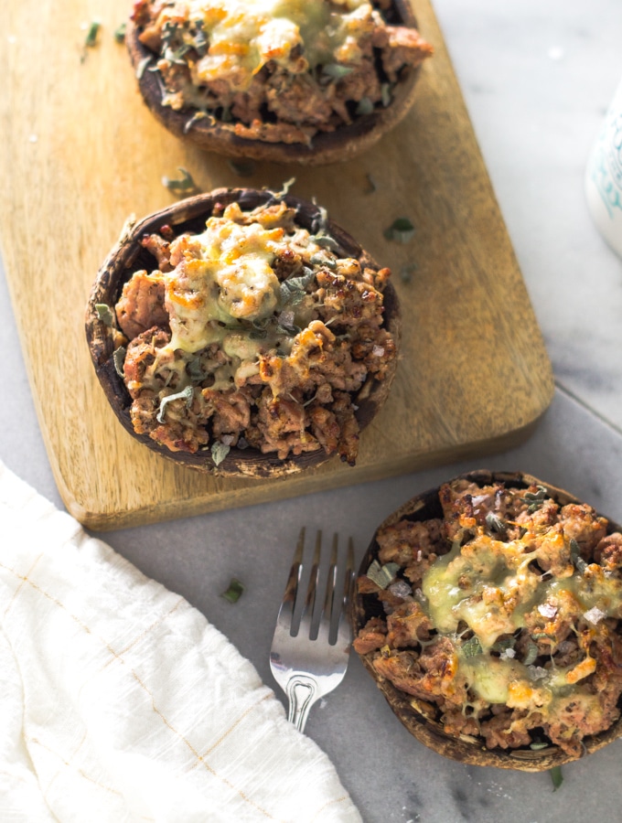 Three large portobello stuffed mushrooms with spiced sausage one a cutting board with a fork and a white napkin